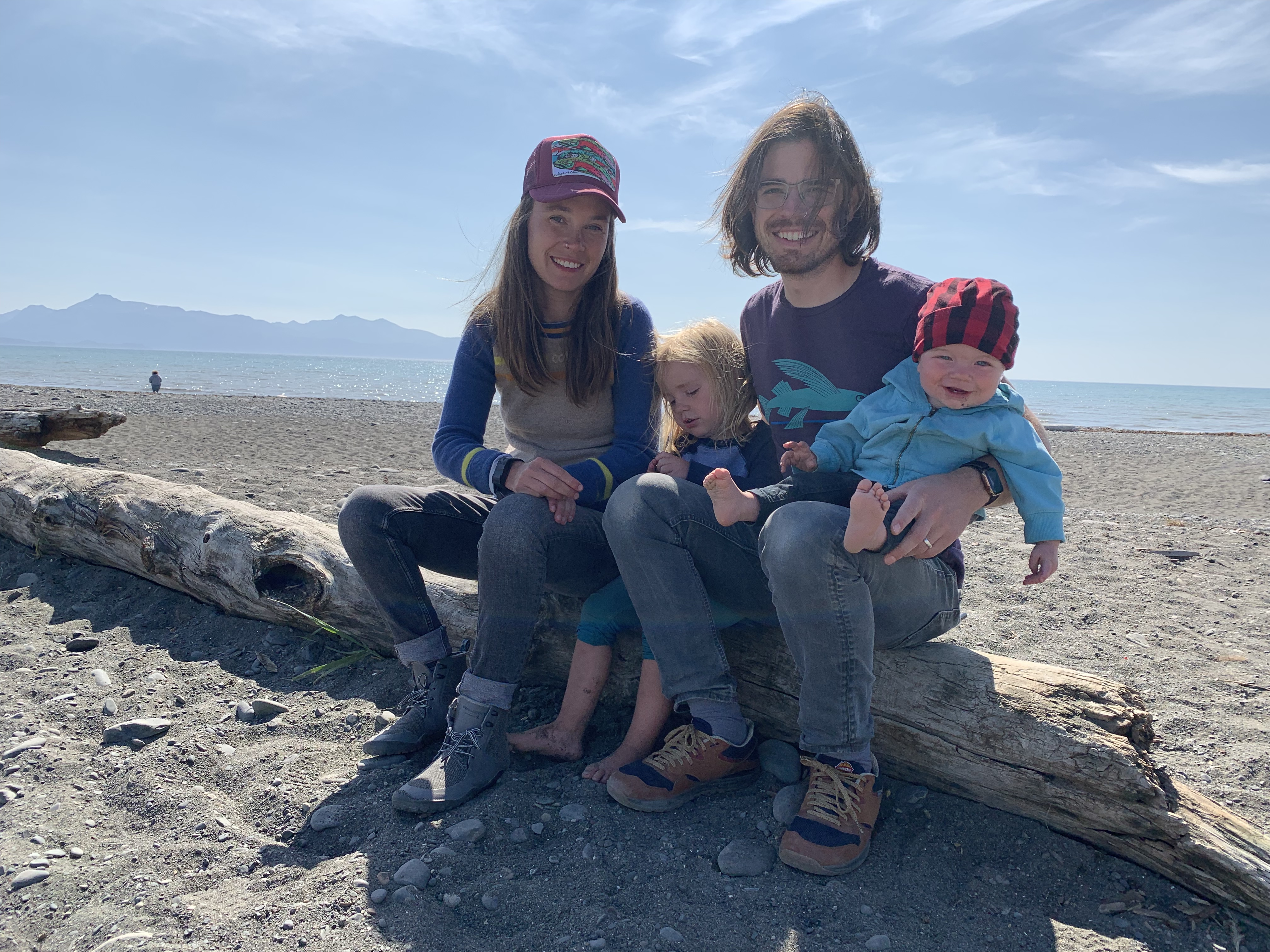 Alex with her husband and two children, sitting on a deadwood log at the beach