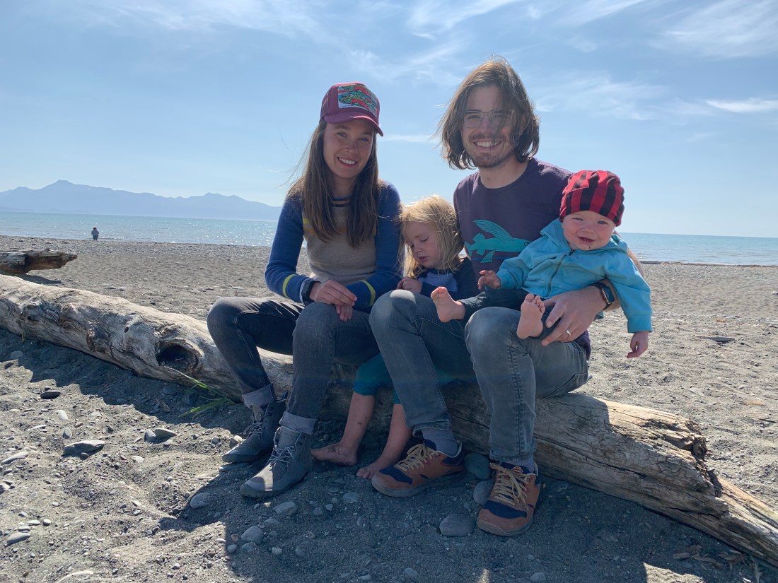 Alex with her husband and two children, sitting on a deadwood log at the beach